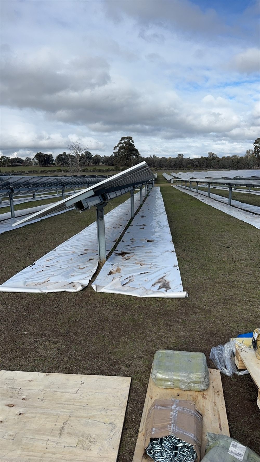 Portrait view between two rows of tracker racking with the Sunplus mat installed on the ground, hardware packages in the foreground.