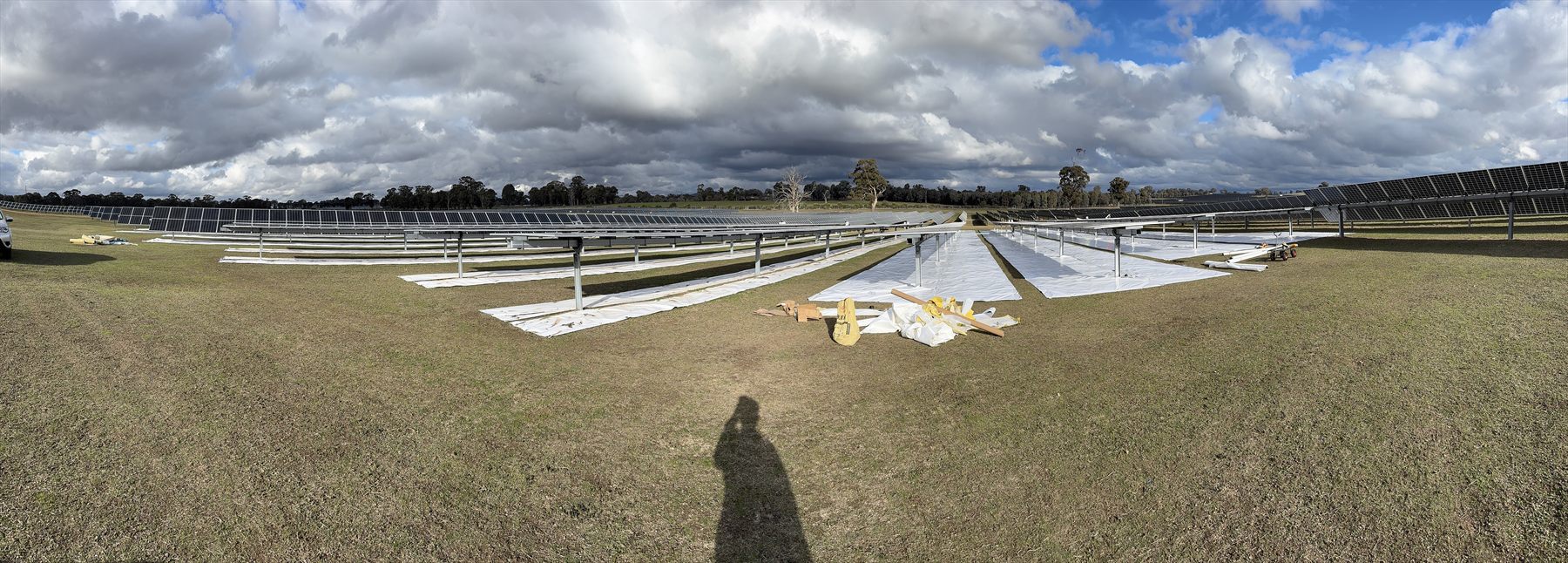 Panoramic view of an Australian single-axis tracker array with Sunplus reflective mat laid between the rows under a cloud-scattered sky.