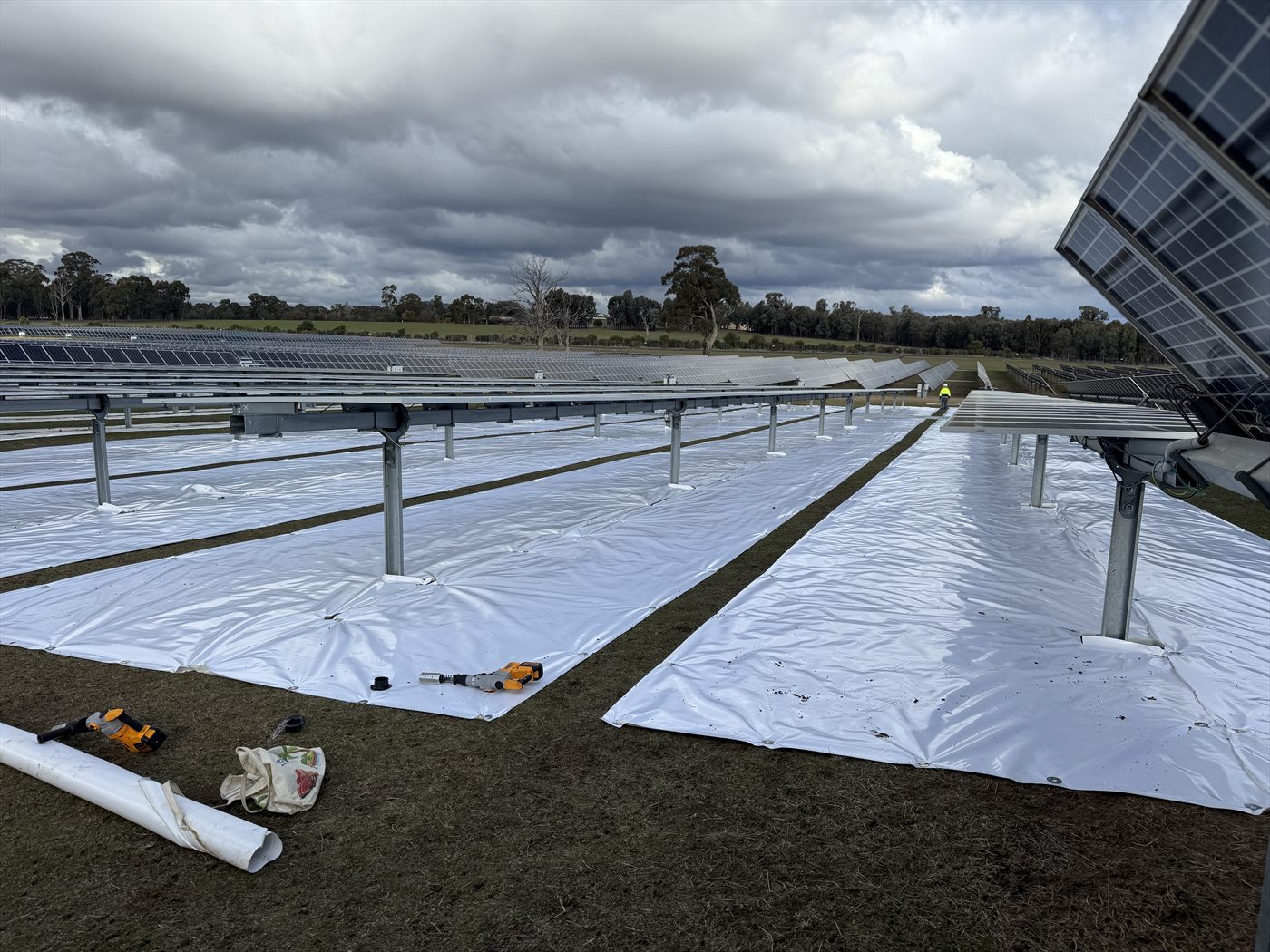 Close ground-level view of Sunplus mat rows during install in Australia, with hand tools on the mat and tracker racking above.
