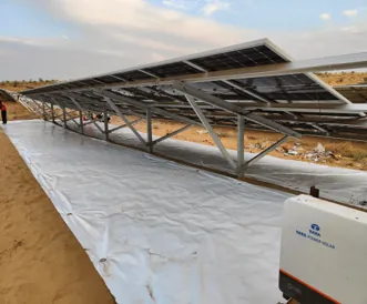 Sunplus matting being laid beneath a newly erected steel racking structure on sandy ground.