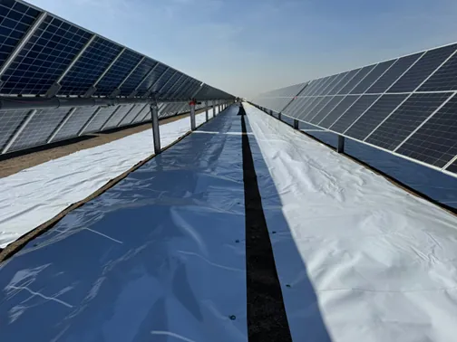A mirror-bright Sunplus mat laid the full length of the inter-row gap between two rows of bifacial modules at a desert site, reflecting the sky.