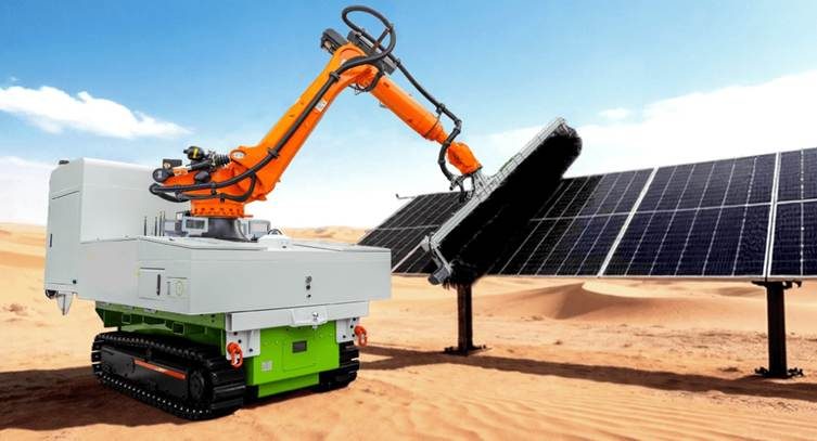 A robotic solar-panel wet-cleaner — an articulated arm mounted on a tracked chassis — brushing a row of bifacial modules at a large desert PV site.